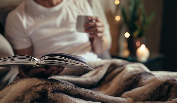 Mann mit Buch und Tee im Bett Entspannung als Einschlafhilfe