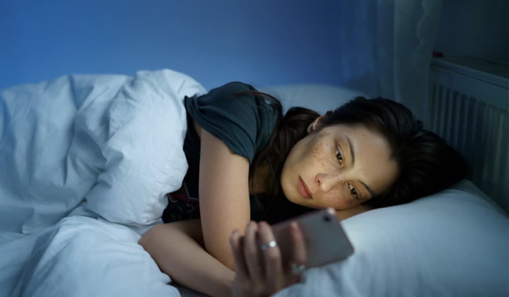 Frau am Handy im Bett Einschlafstörungen