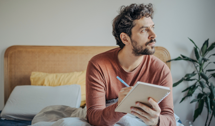 Mann sitzt im Bett und führt Schlaftagebuch