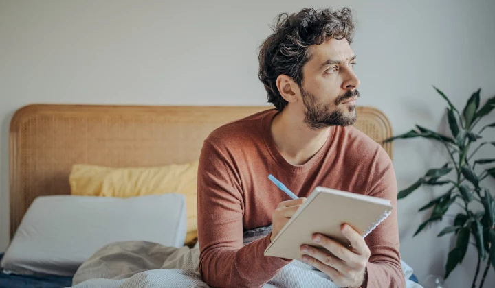 Mann sitzt im Bett und führt Schlaftagebuch Mann sitzt im Bett und führt Schlaftagebuch